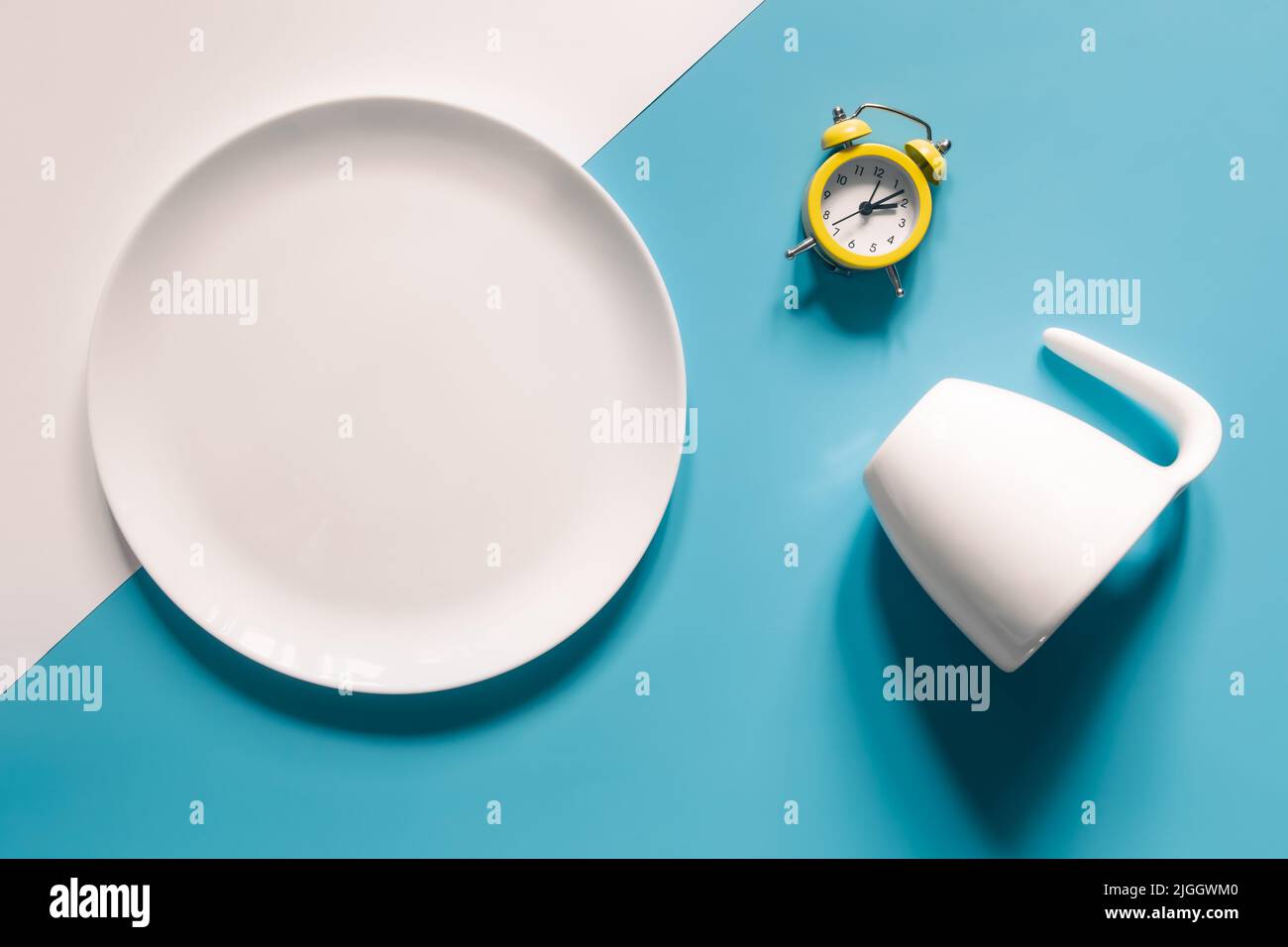 Empty plate, cup and alarm clock on a blue background. Stock Photo