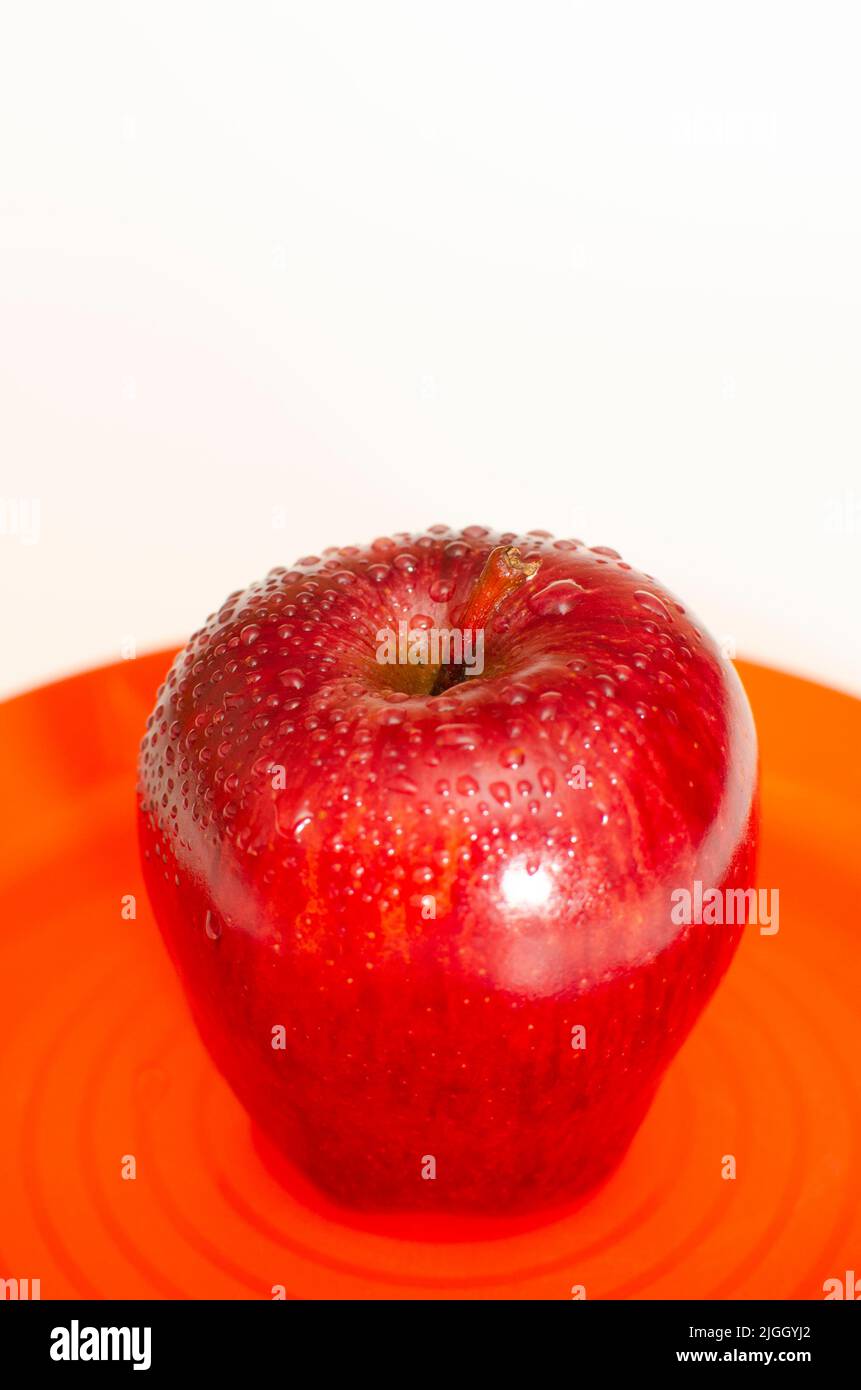 Fresh red apple in orange coloured plate on the white background Stock Photo