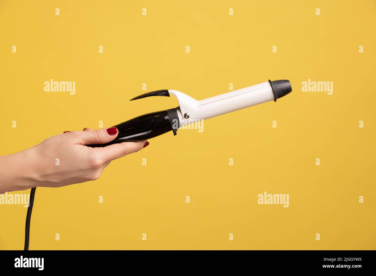 Closeup side view of woman hand holding showing iron curler, professional curling tongs, beauty
