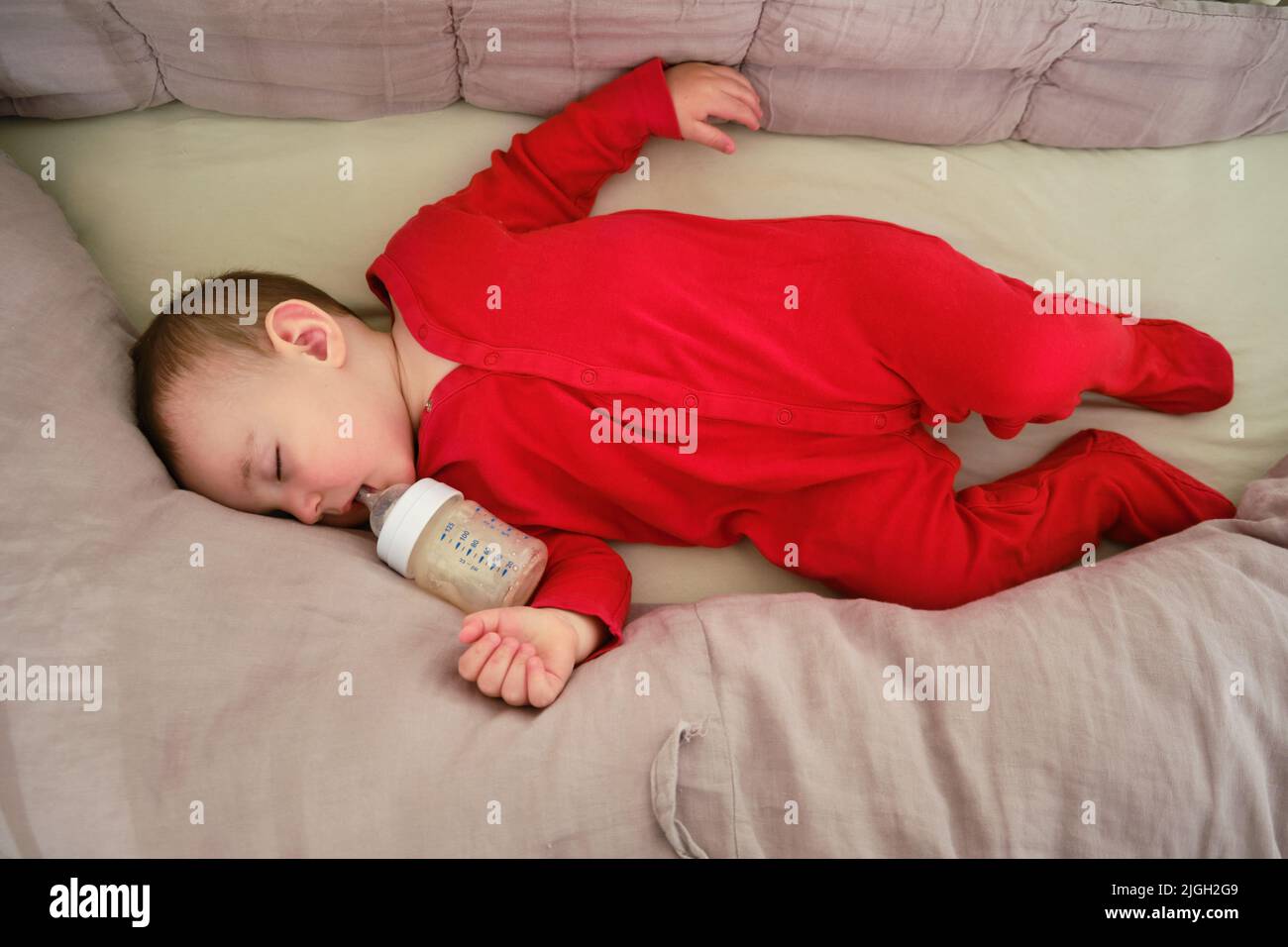 Toddler baby sleeps in a crib with a bottle of milk formula in his