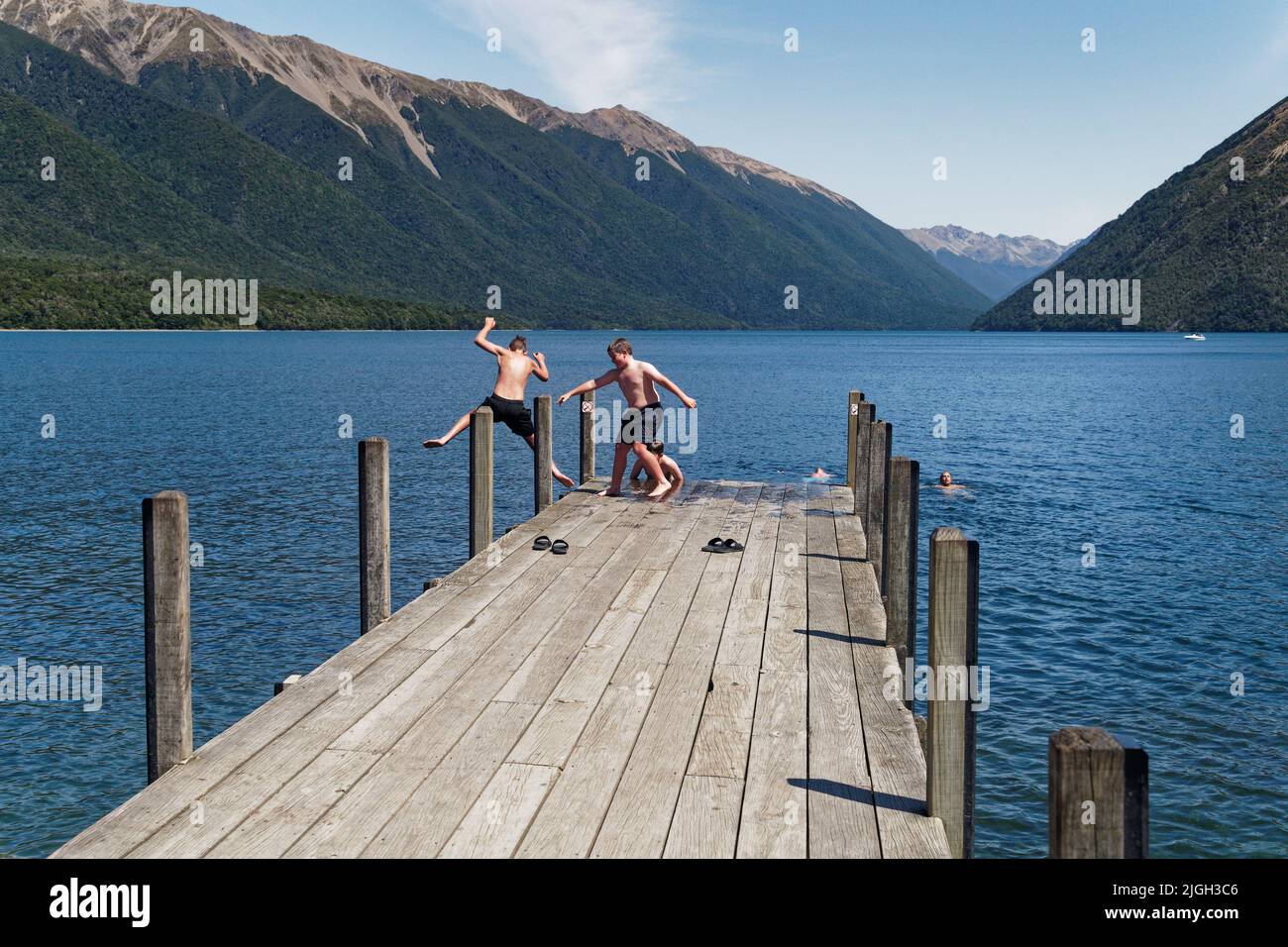 Nelson Lakes National Park, New Zealand - January 24, 2020: Summer holidays, boys jumping off the jetty and people swimming at Lake Rotoiti, Aotearoa Stock Photo