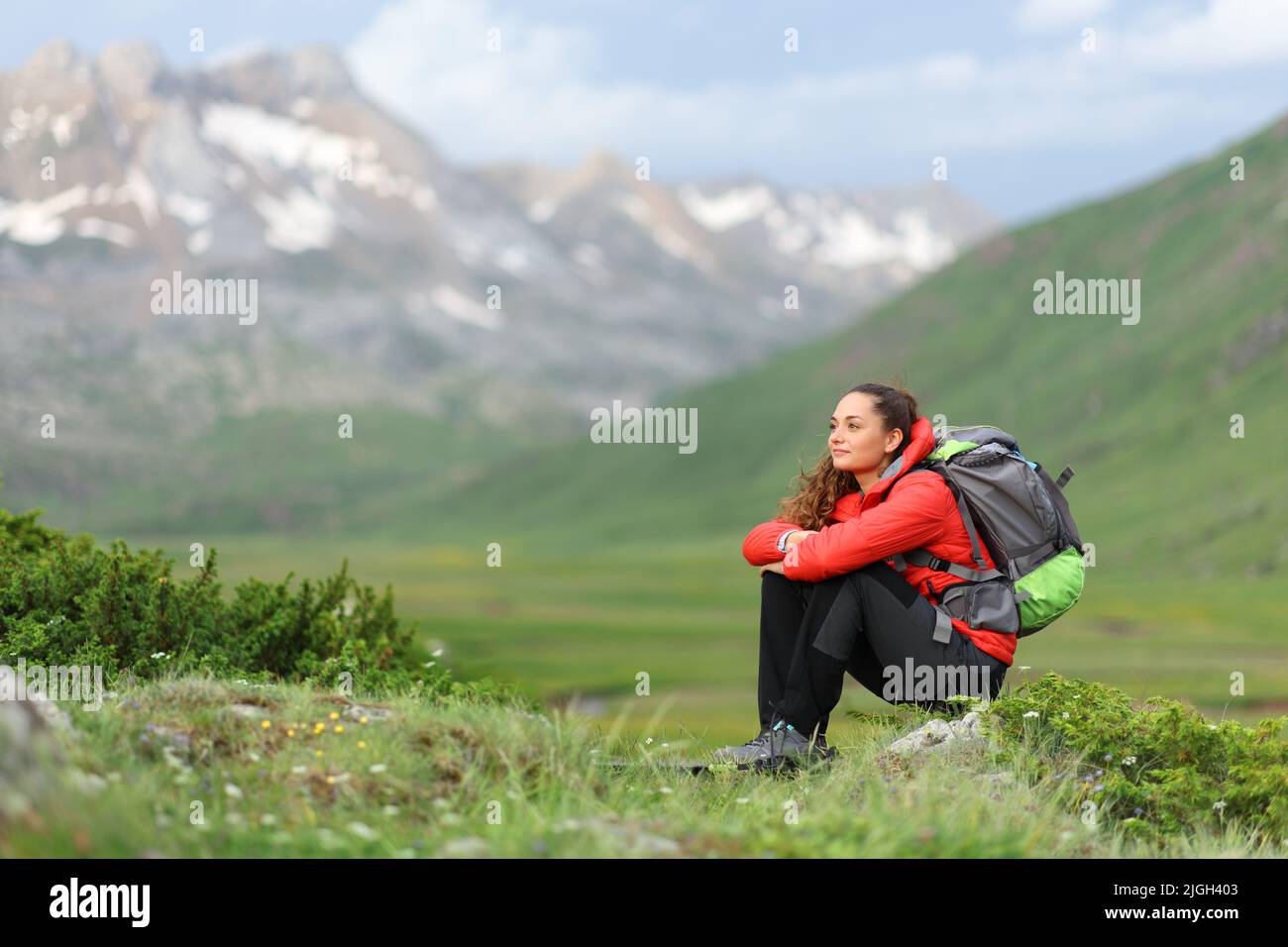 Hiker in red sitting contemplating views in a green mountain Stock Photo