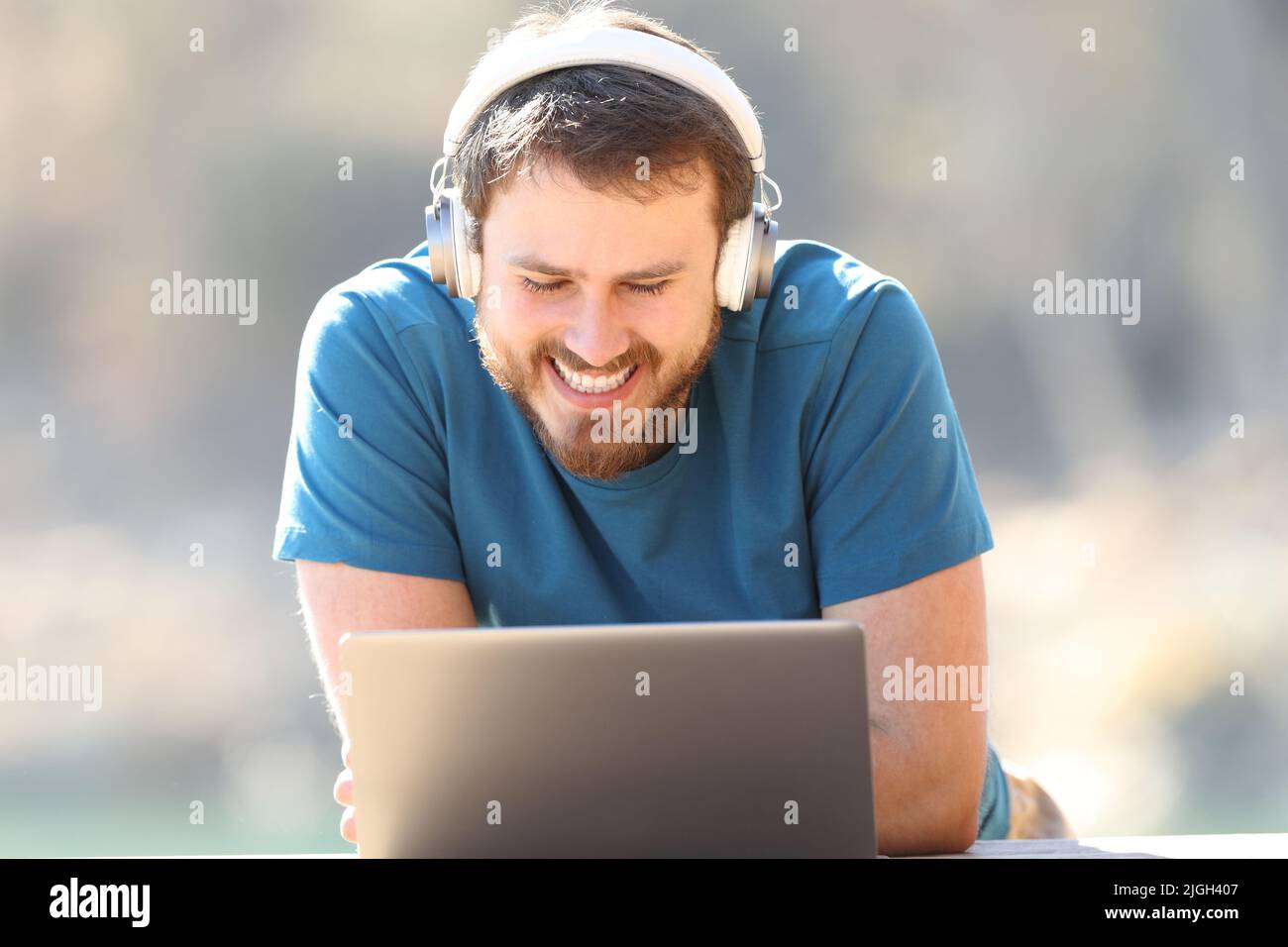 Front view of a happy man watching videos on laptop wearing headphones outdoors Stock Photo
