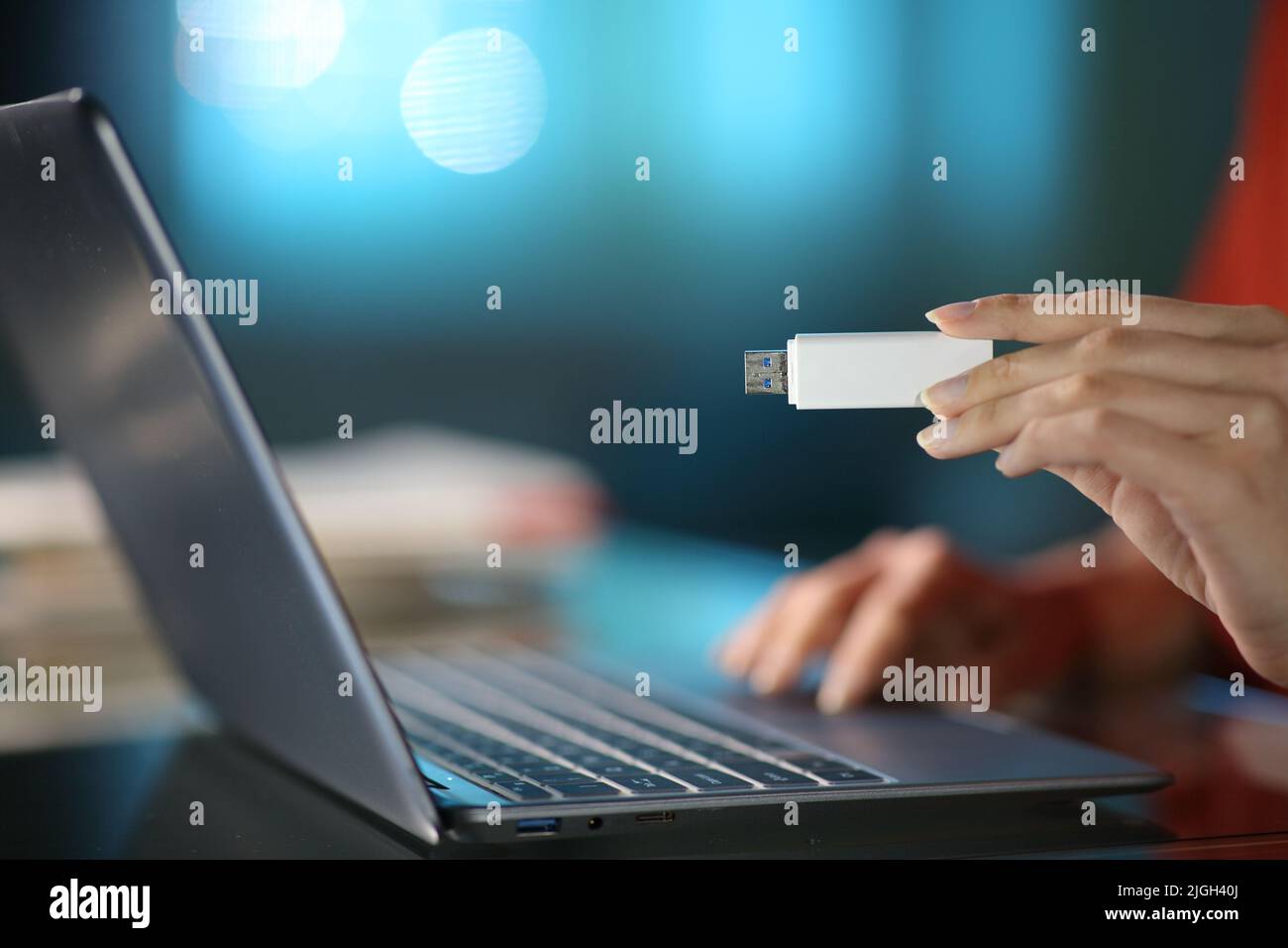 Close up of a woman using a laptop with her hand holding a pen drive in the night at home Stock Photo