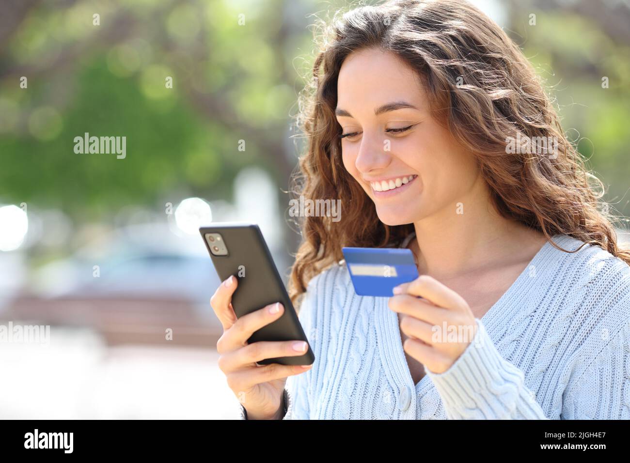 Happy woman buying online with credit card and cell phone in the street Stock Photo