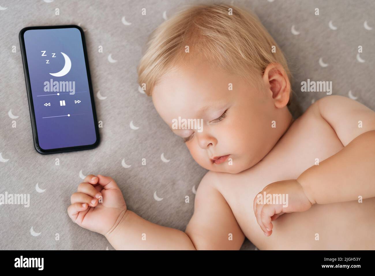 Closeup portrait of cute little boy watching sweet dreams in his bed falling asleep with music playing in app for baby sleep on phone lying next to his head. Happy maternity and technology Stock Photo