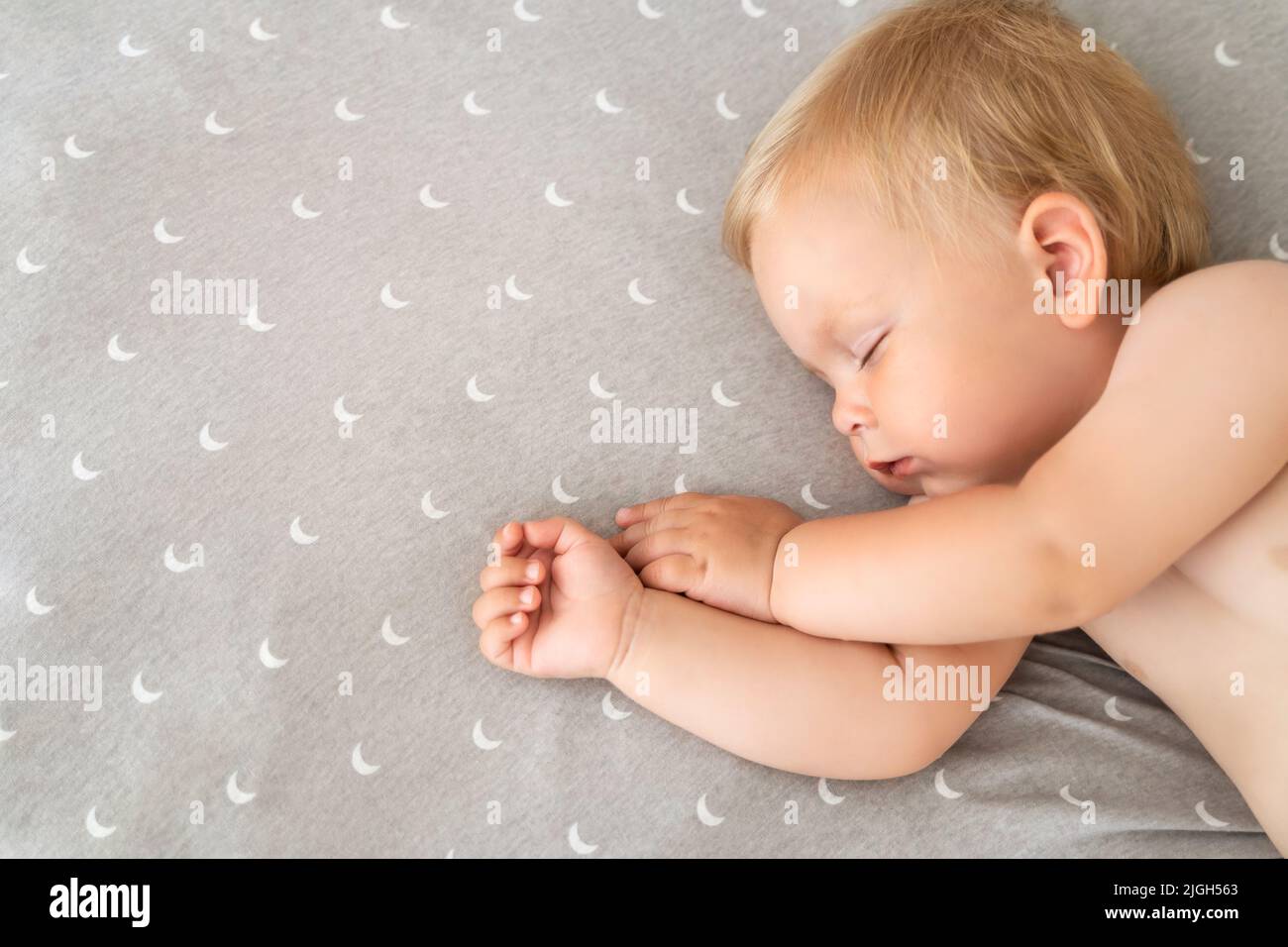 Close up indoor portrait of cute baby sleeping in bed with copy space for your advertising content on the right , watching sweet dreams after active play outside. Nap time. Childcare. Stock Photo