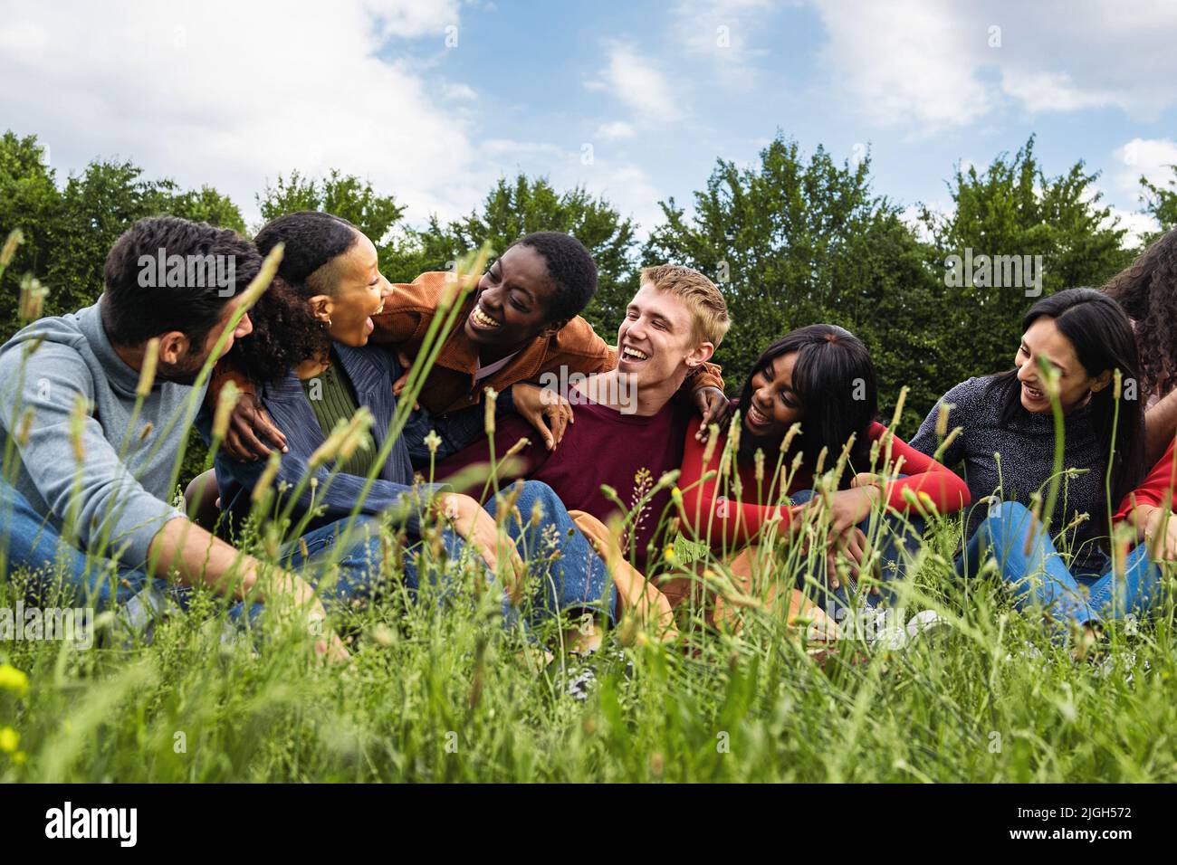 Multiracial community of gen z happy friends having fun sitting in the grass - concept of multiethnic youth culture, diversity, oneness, trust Stock Photo