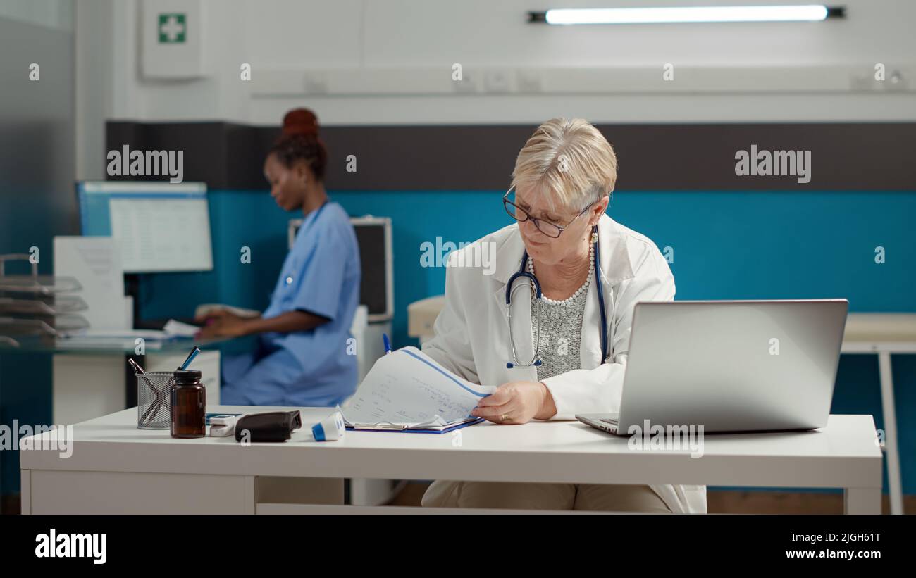 General practitioner working with appointment report on laptop, using diagnosis information to