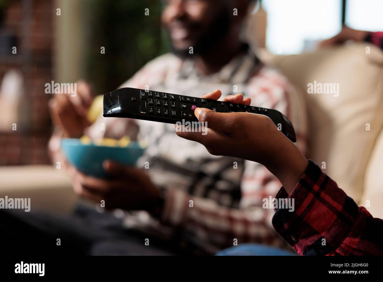 Girlfriend holding tv remote control to switch channel program and find movie on television to watch. Eating takeaway delivery from fast food and watching film together. Close up. Stock Photo