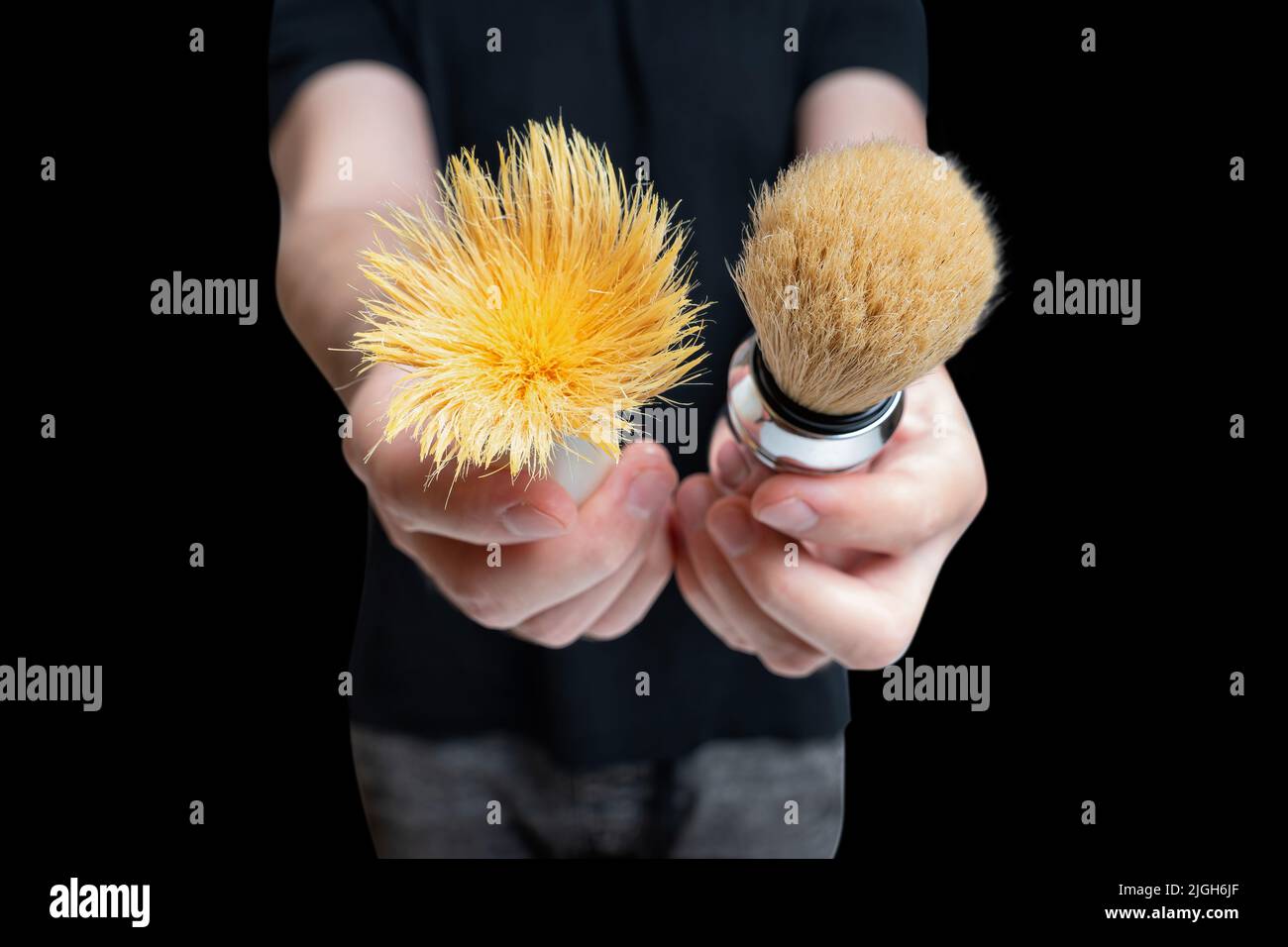 Male demonstrating a worn shaving brush close to a fresh one isolated