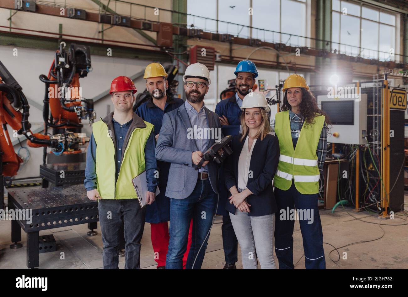 Young man worker with Down syndrome with manager and other collegues working in industrial factory, social integration concept. Stock Photo