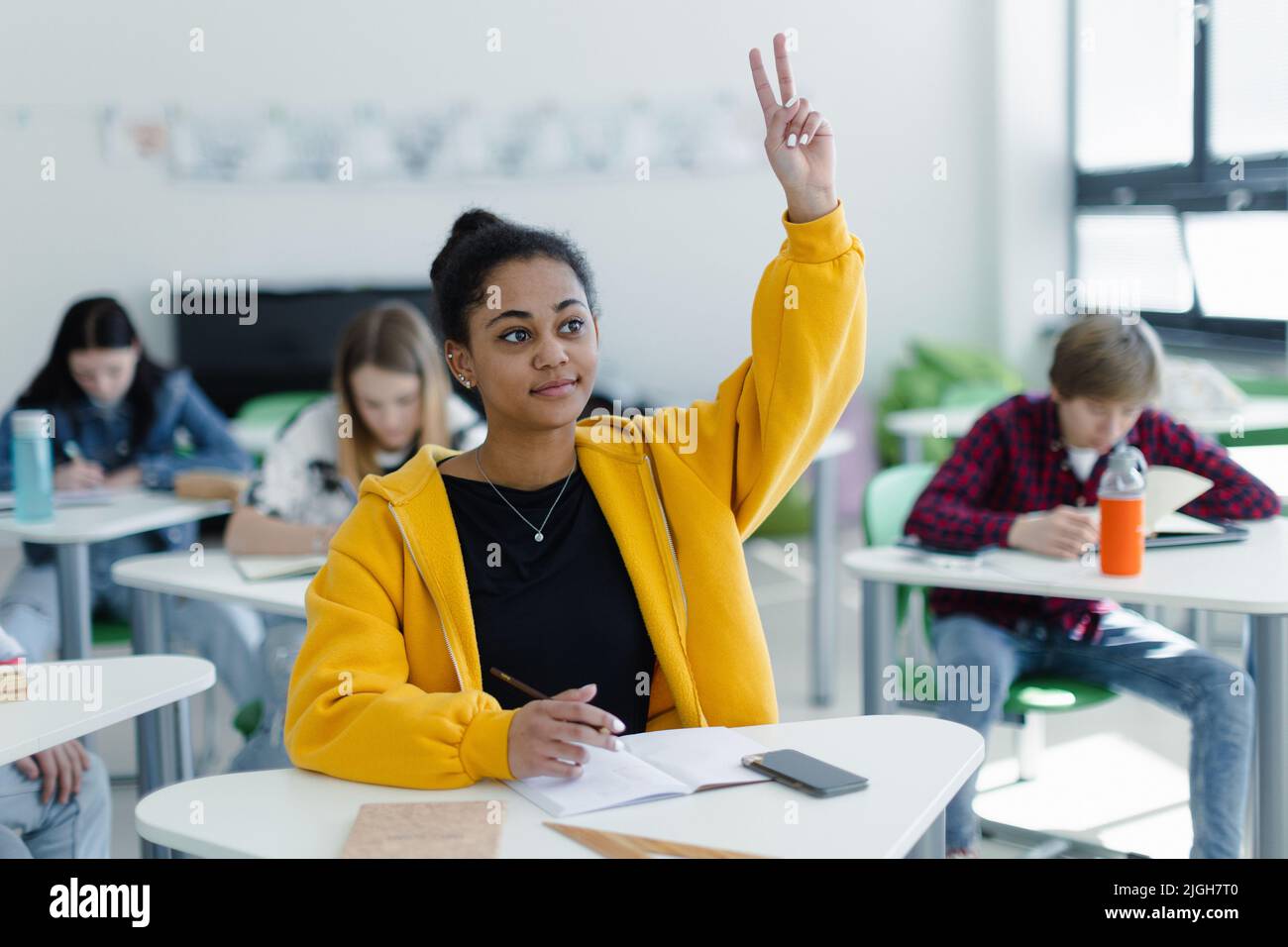 High school students paying attention in class, sitting in their desks and raising hand. Stock Photo