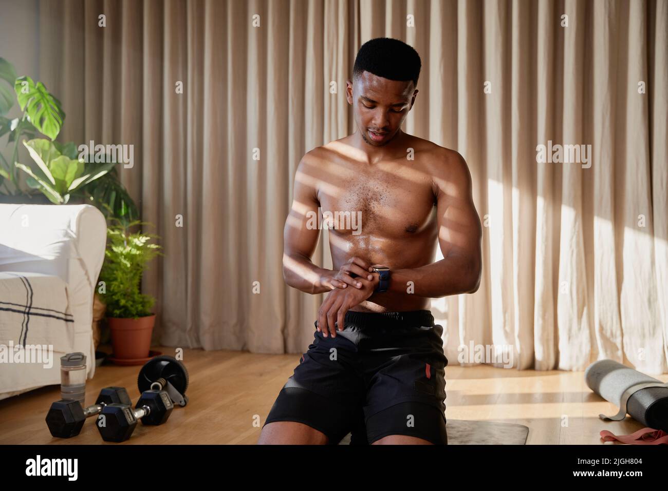 African American young black male working out at home checking sports watch and about to start his exercise on his yoga mat in his living room Stock Photo
