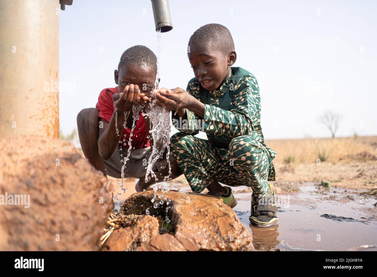 Two happy boys playing with fresh water from a village tap in an African steppe region; desertification progress and water scarcity concept Stock Photo