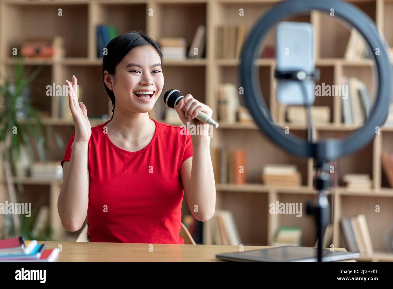 Satisfied young japanese lady with microphone sings at microphone in karaoke and shoots video for blog Stock Photo