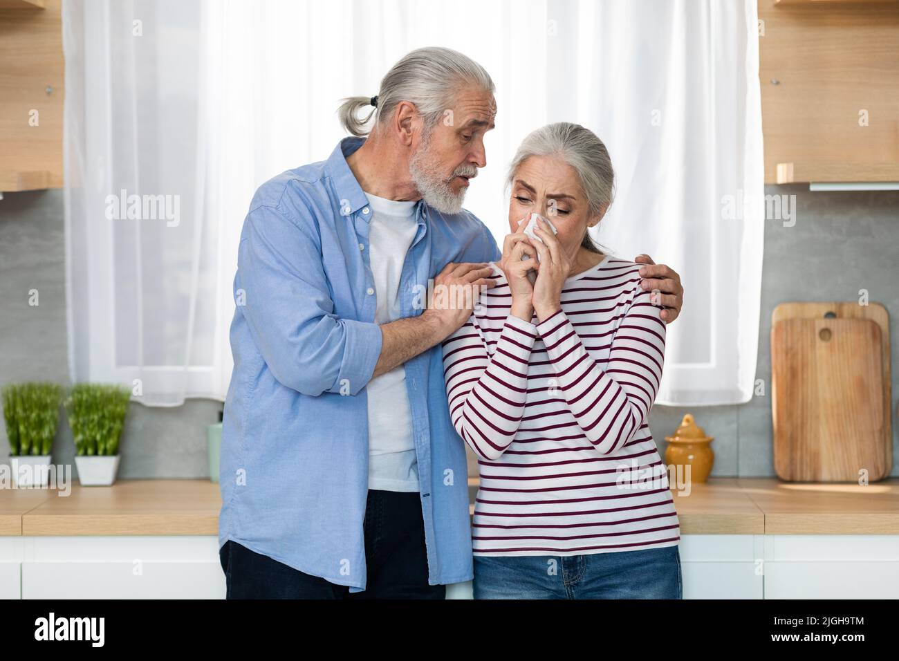 Caring Senior Man Comforting His Crying Wife In Kitchen At Home Stock Photo