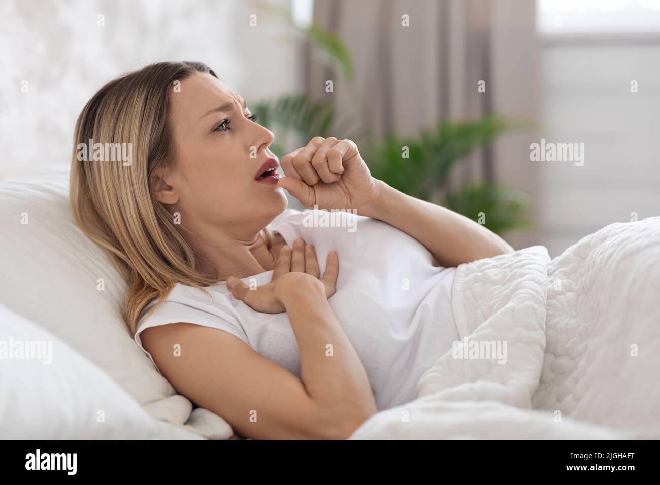 Ill blonde lady coughing and touching her chest Stock Photo Alamy