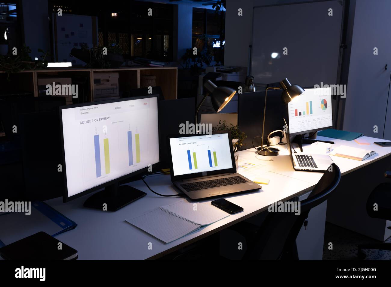 Computers with laptops, illuminated pendant lights, smartphone and diaries on desk in modern office Stock Photo