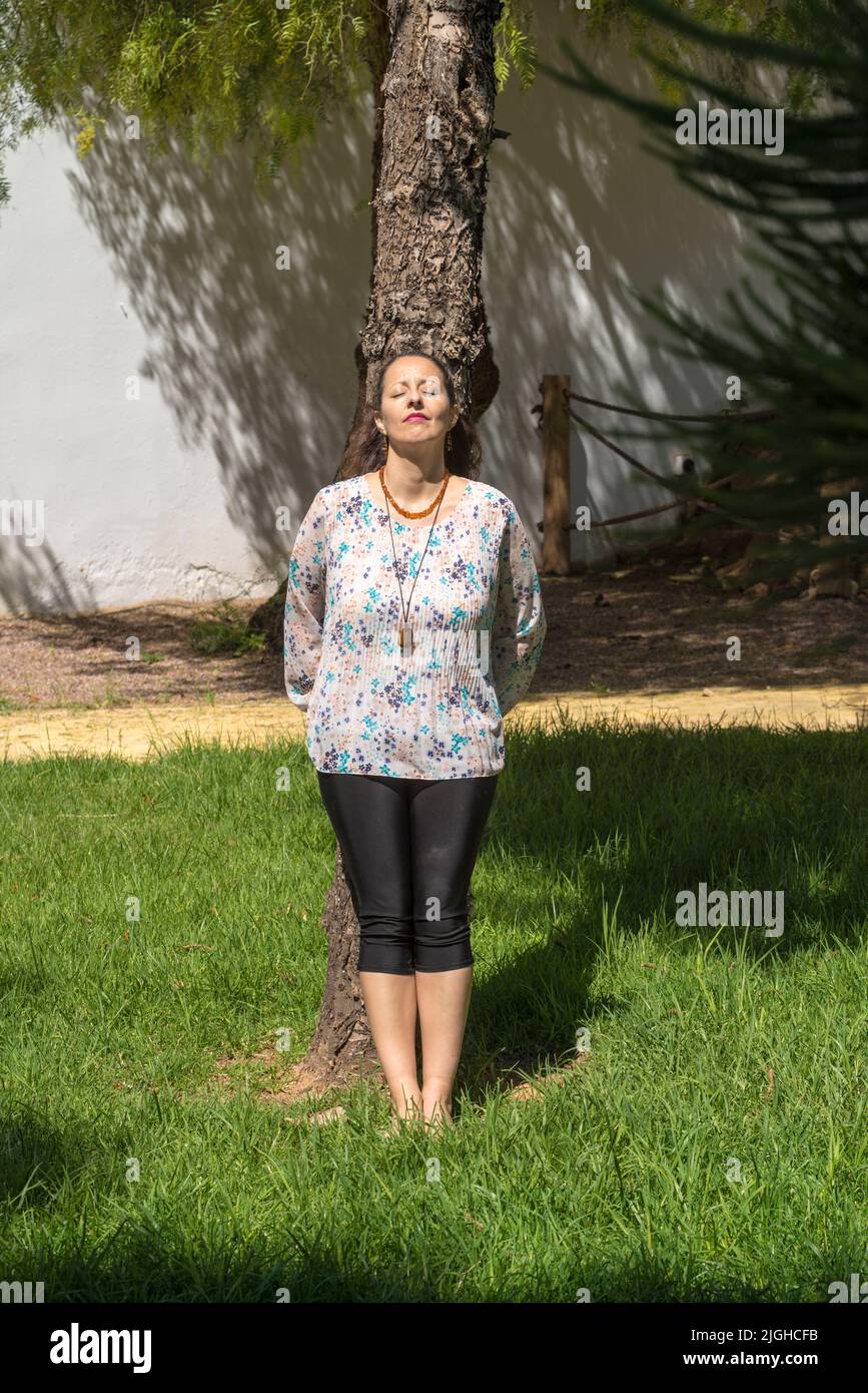 A woman sunbathes standing and hugging a tree. Hugging a tree has many