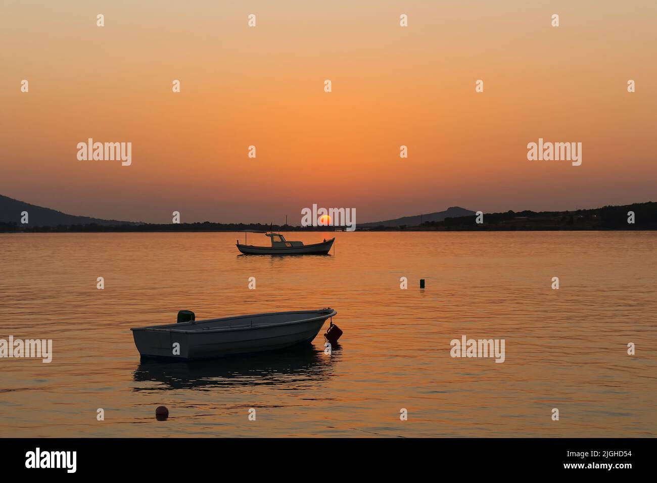 View of small, wooden fishing boats, Aegean sea and landscape at sunset captured in Ayvalik area of Turkey in summer. Beautiful scene. Stock Photo