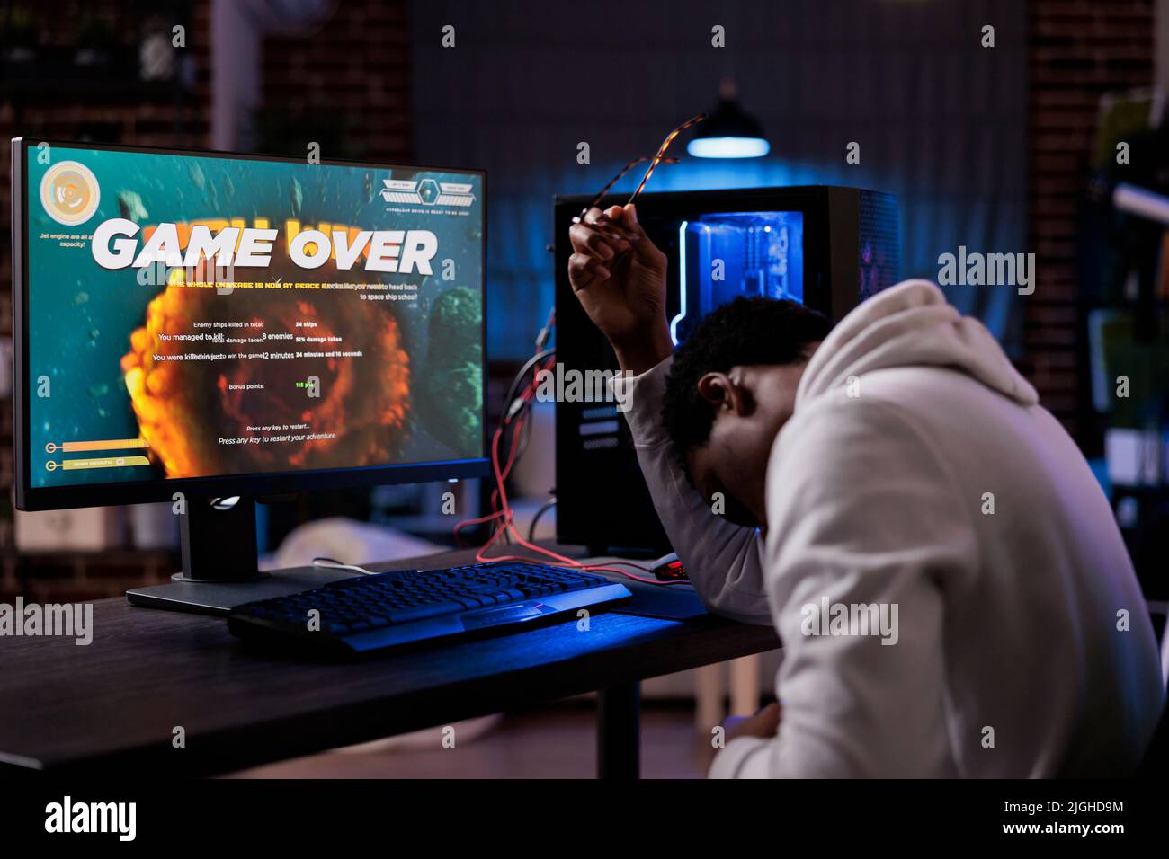 Frustrated streamer losing online shooter video games play competition on computer with neon lights. Male gamer streaming action gameplay and feeling sad about lost shooting championship. Stock Photo