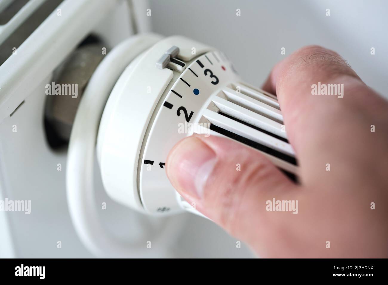 person adjusting thermostat on radiator to lower temperature, saving energy and money concept Stock Photo