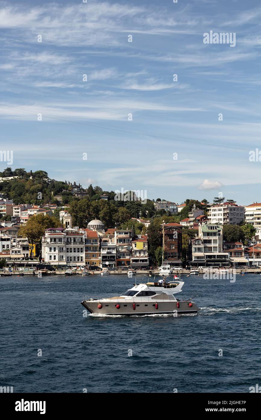 View of a yacht passing on Bosphorus by Arnavutkoy neighborhood on European side of Istanbul. It is a sunny summer day. Beautiful travel scene. Stock Photo