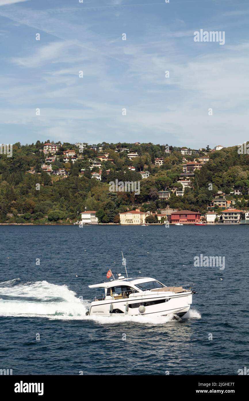 View of a yacht passing on Bosphorus and Asian side of Istanbul. It is a sunny summer day. Beautiful travel scene. Stock Photo