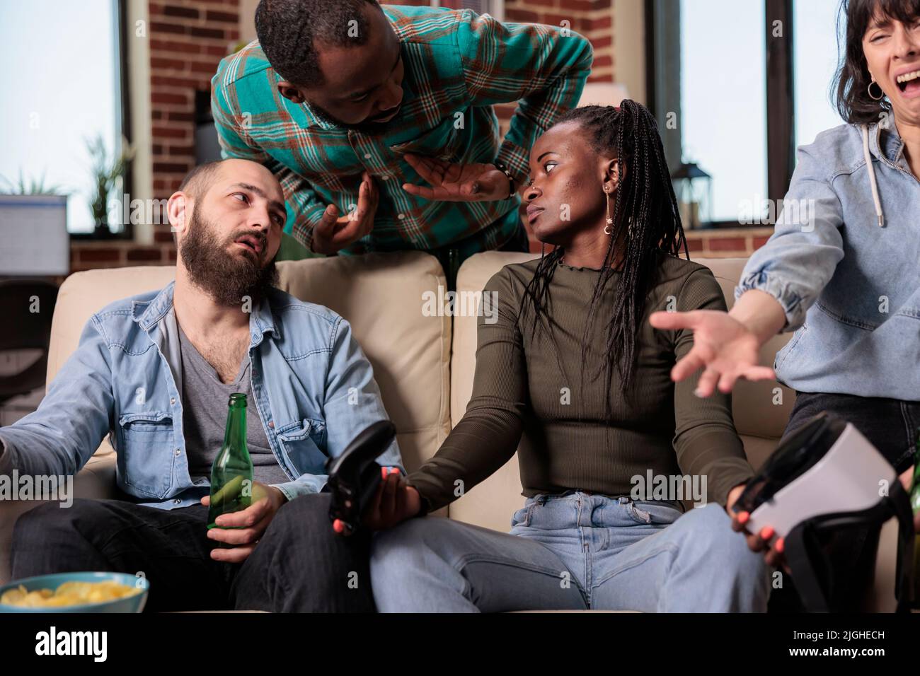 Multiethnic group of friends winning video games with vr goggles , feeling sad about lost competition with augmented reality glasses. Enjoying gathering with people together with alcoholic drinks. Stock Photo