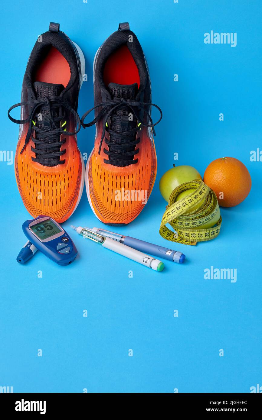 Orange sneakers, fruits, measuring tape, glucometer and insulin syringe pens on a blue background. Exercise, nutrition and diabetes management Stock Photo