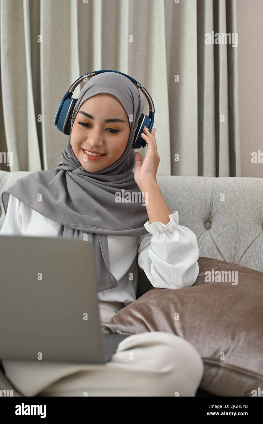 Beautiful young Asian Muslim woman wearing hijab and headphones ...