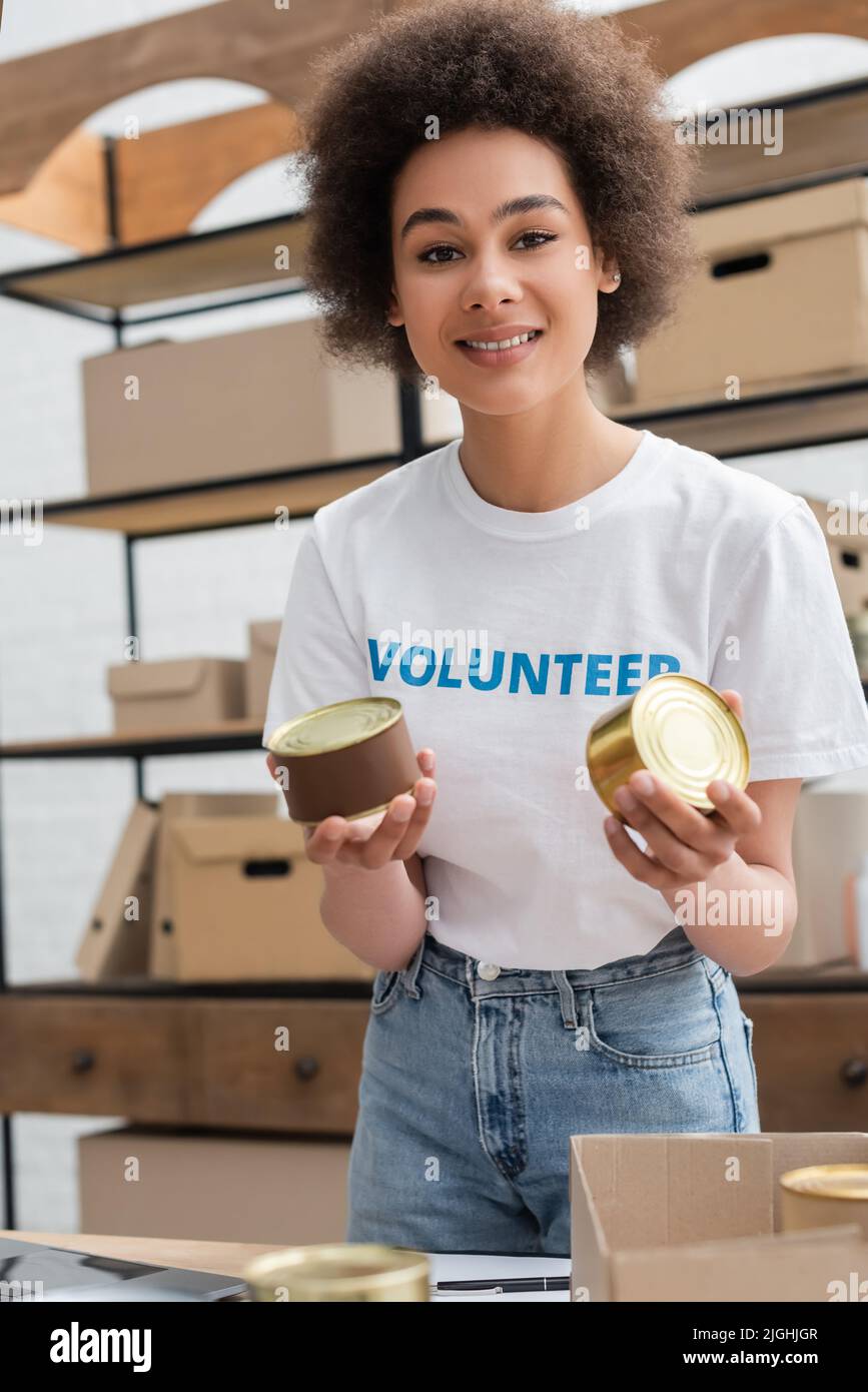 young african american volunteer with canned food smiling at camera in