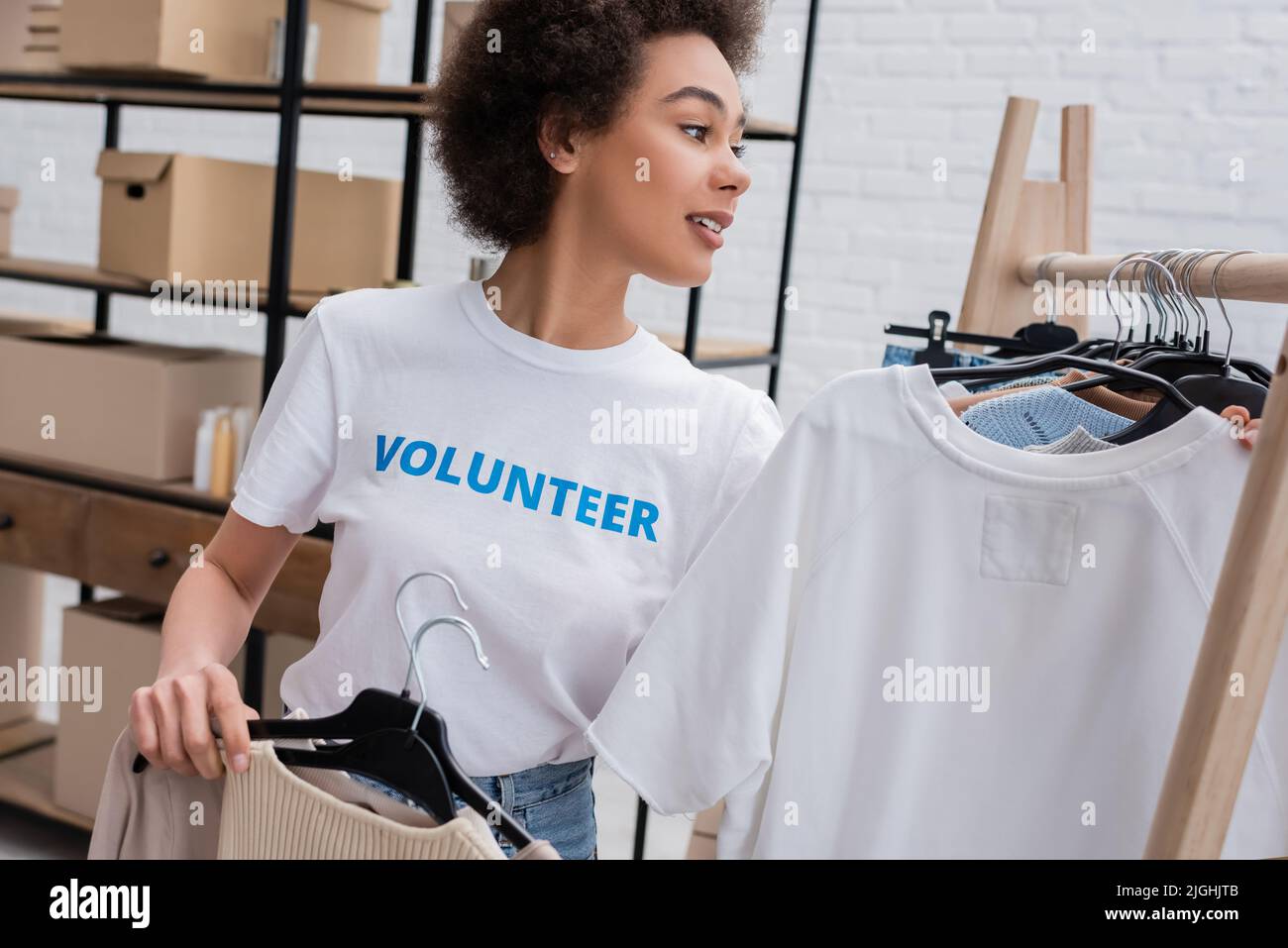 smiling african american volunteer holding hangers with clothes in