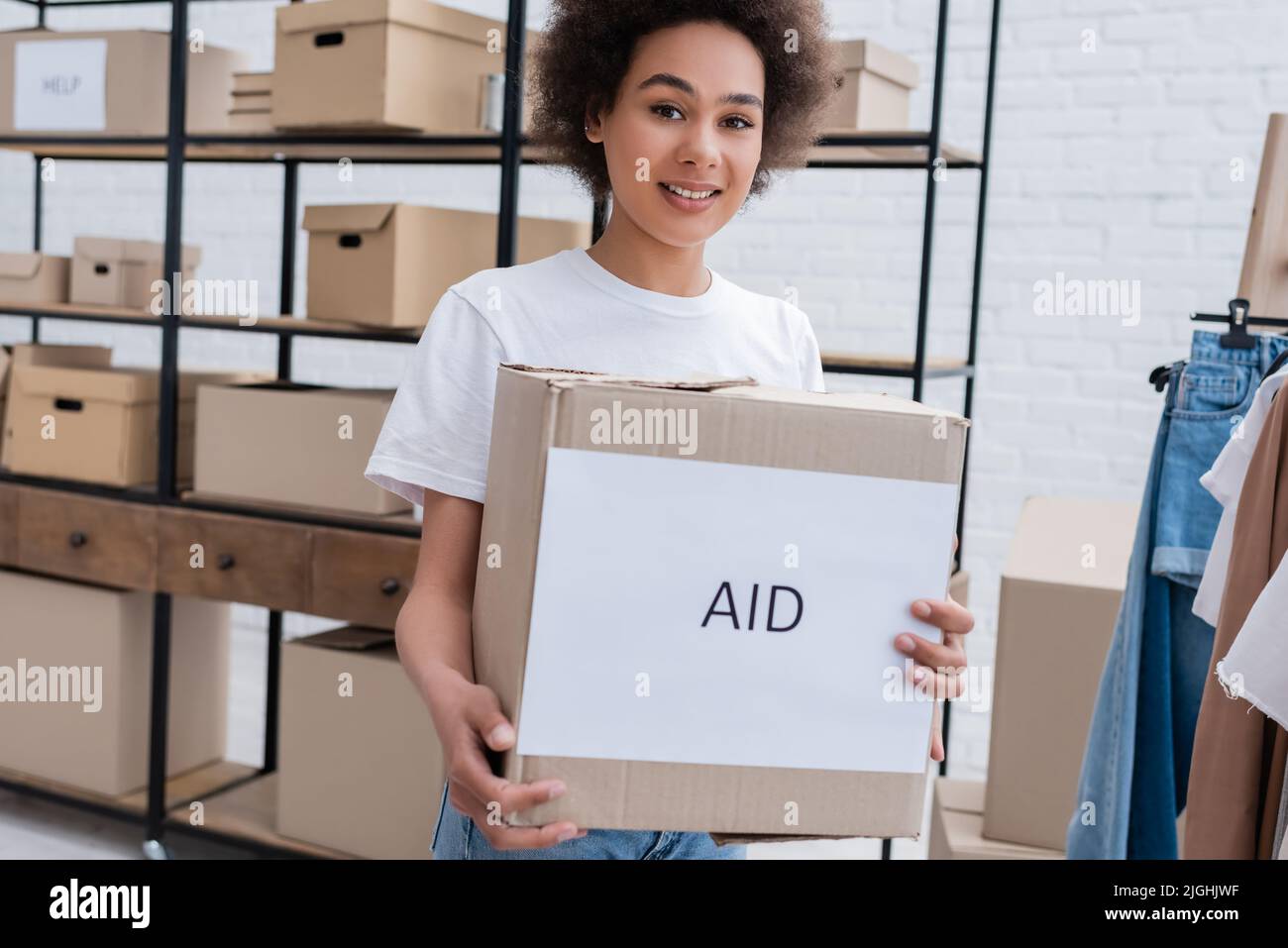 smiling african american volunteer holding box with aid lettering in ...