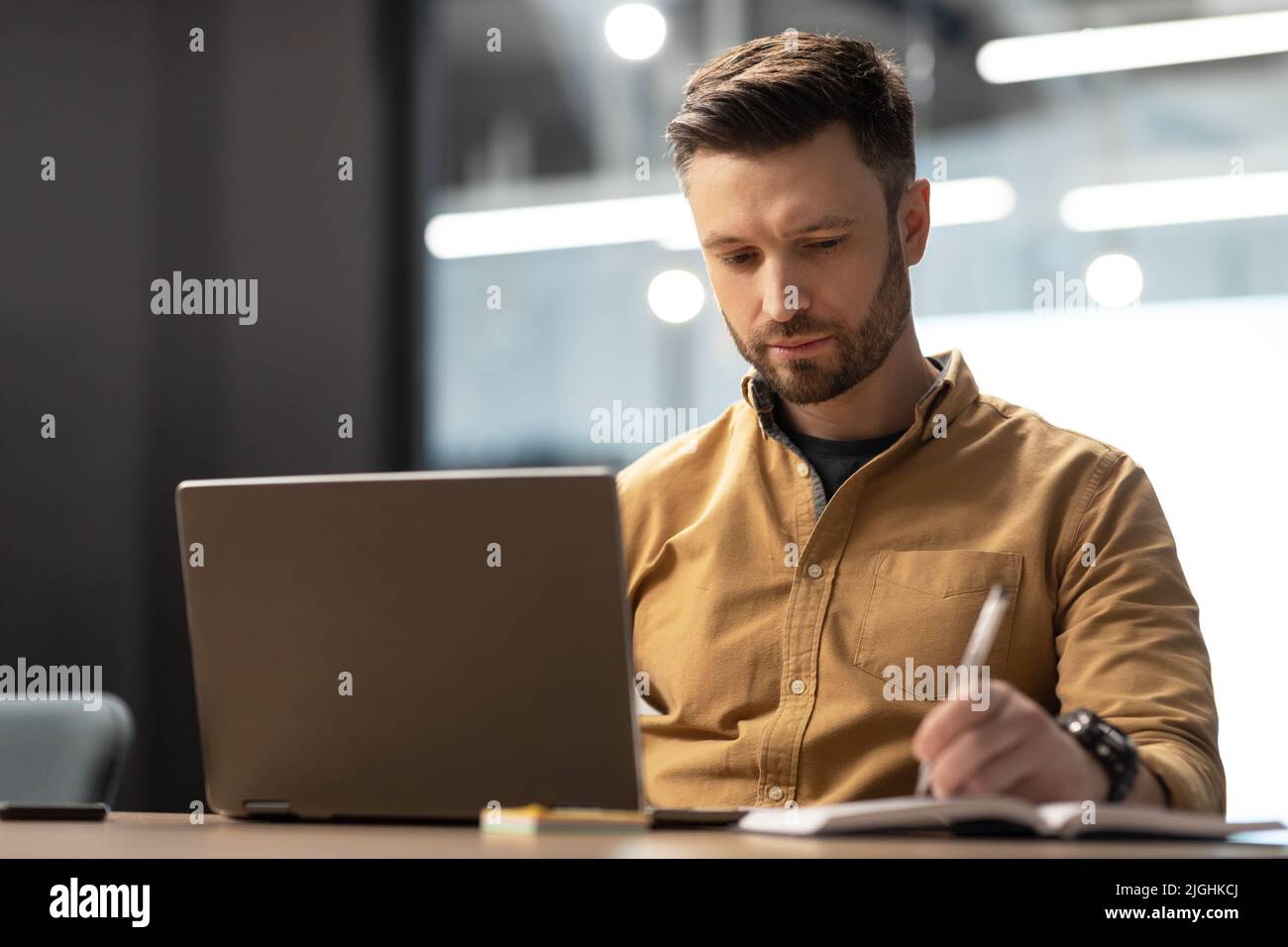 Serious Businessman Using Laptop Computer Taking Notes In Modern Office Stock Photo