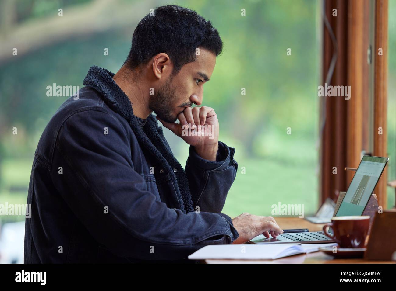 I thought getting out the house would help me crack this. a man using his laptop while sitting in a cafe. Stock Photo