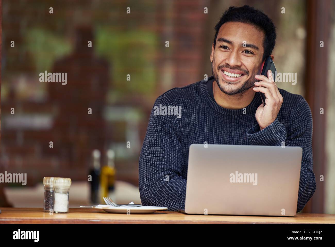 Yes, coming to the cafe was definitely a good idea. a man talking on his cellphone and using his laptop while sitting in a cafe. Stock Photo