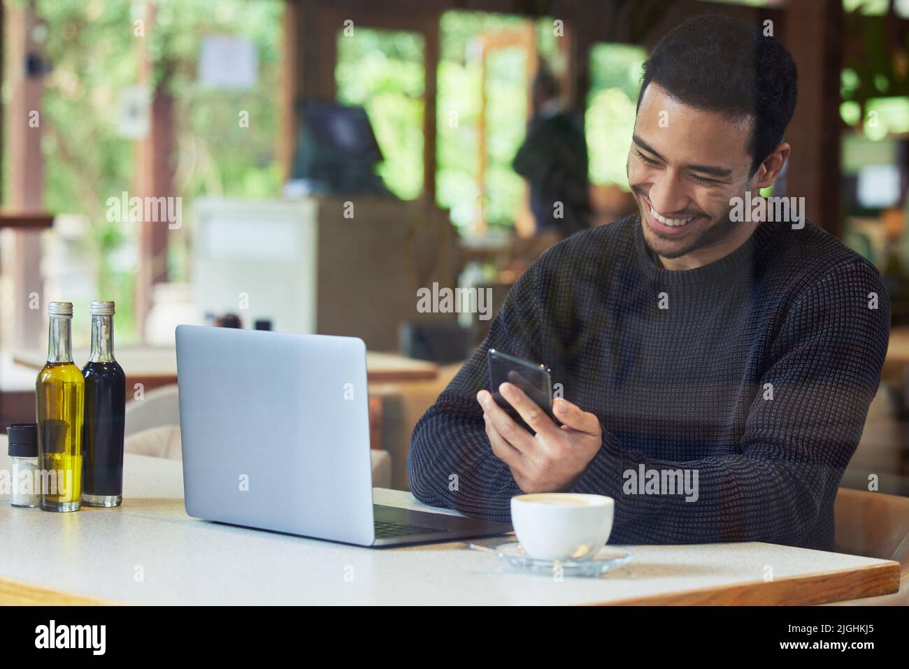 The wifi here gives me the freedom to browse as much as I want. a man using his cellphone while sitting with his laptop in a cafe. Stock Photo