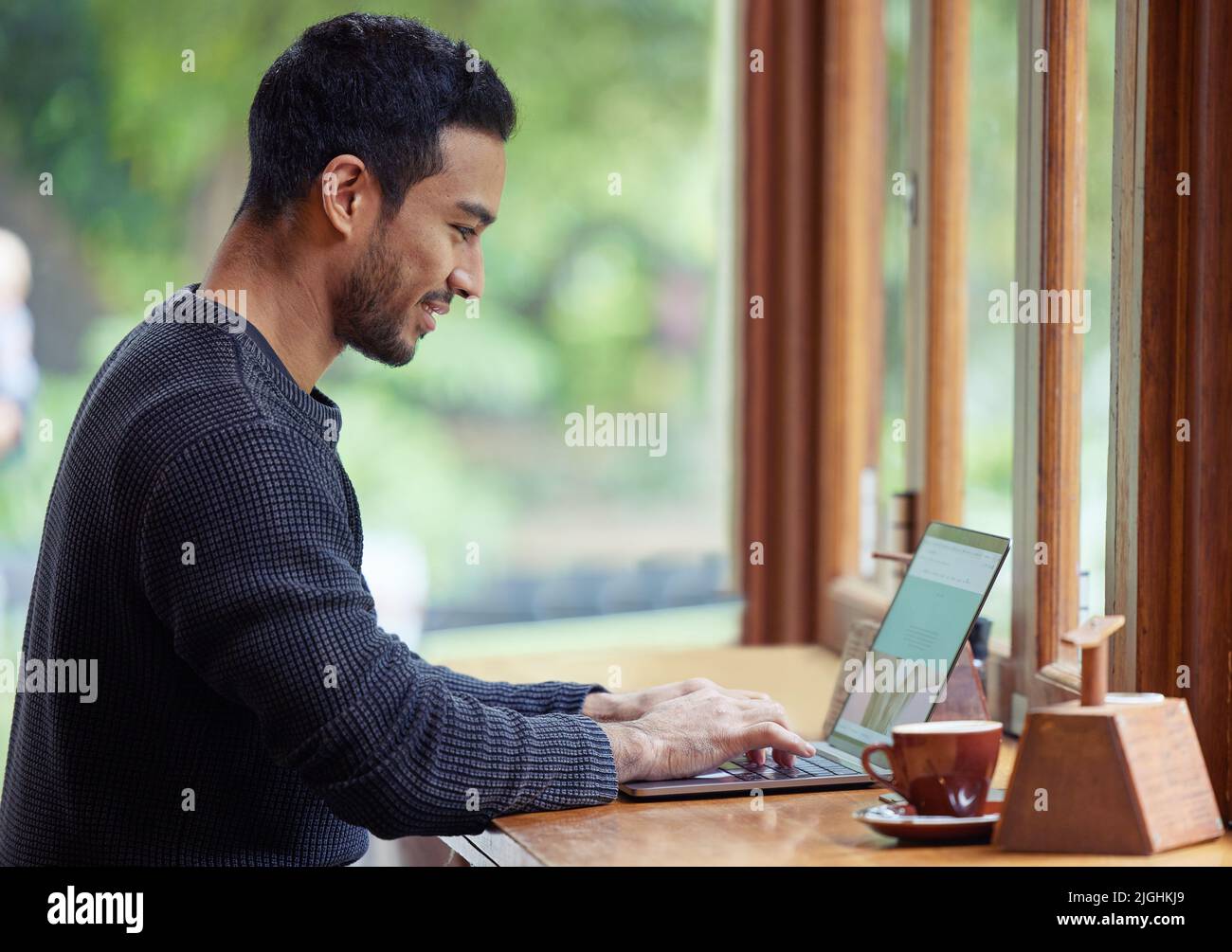 I get to enjoy my coffee and send out a few emails. a man using his laptop while sitting in a cafe. Stock Photo