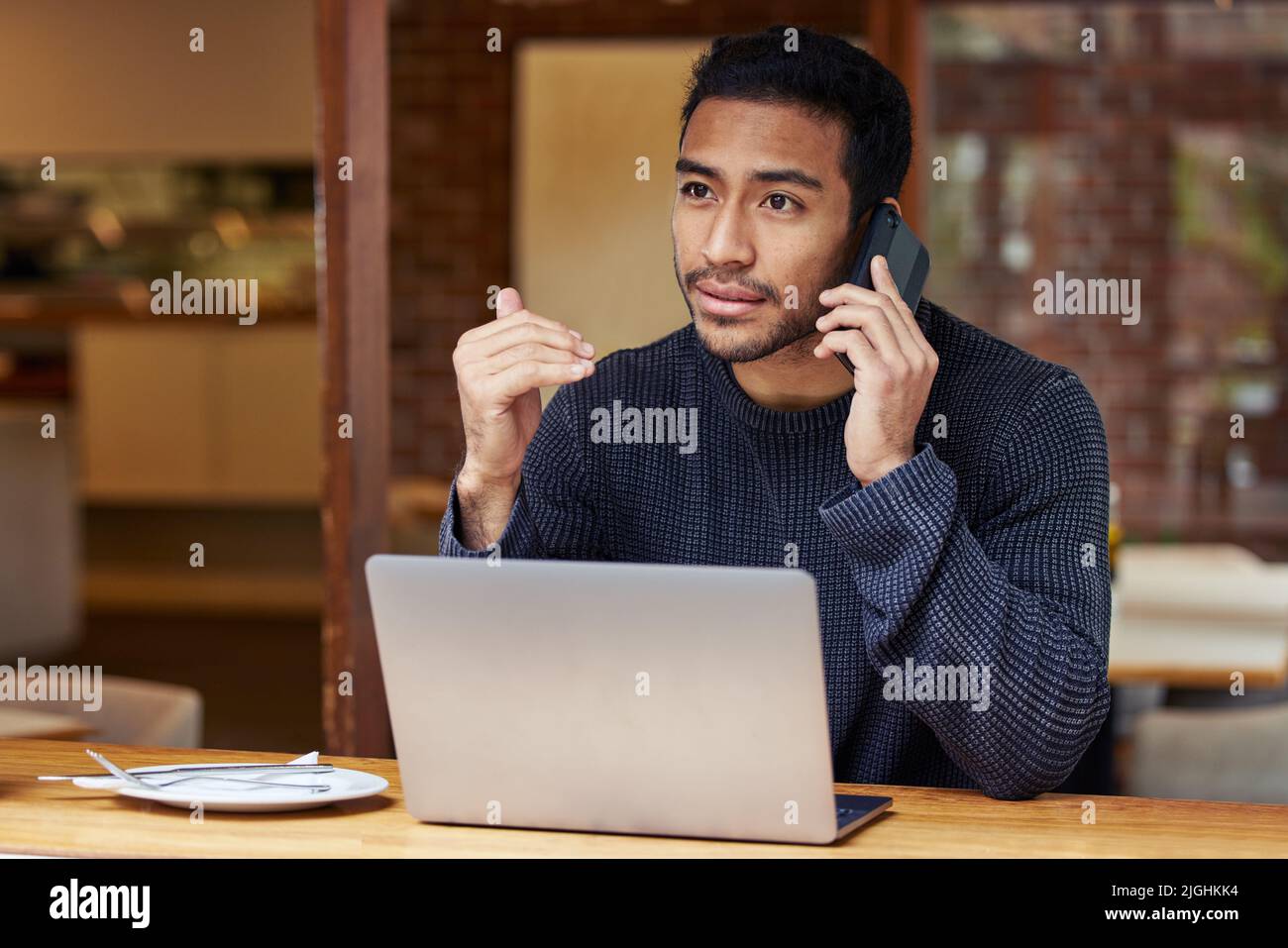 You can meet me at the cafe and we can discuss it. a man talking on his cellphone and using his laptop while sitting in a cafe. Stock Photo