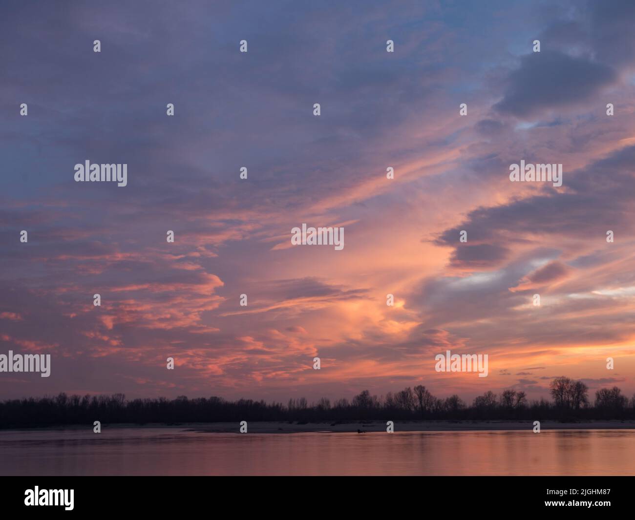 Beautiful pink clouds just after sunset and the silhouettes of trees on the bank of the Vistula River. Poland. Eastern Europe. Stock Photo