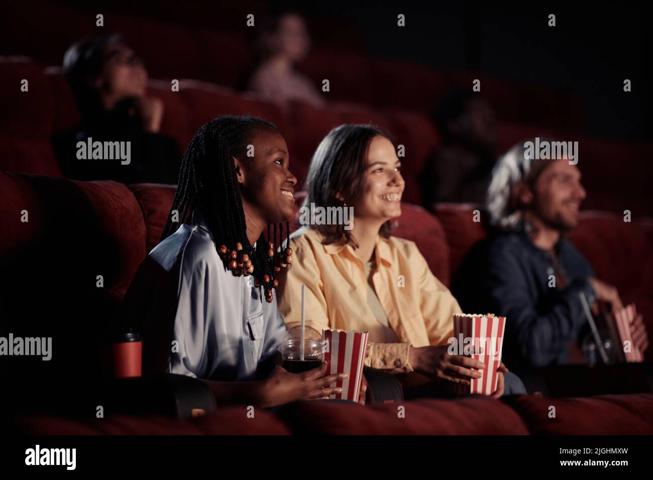Two happy girls eating popcorn and laughing during watching comedy in