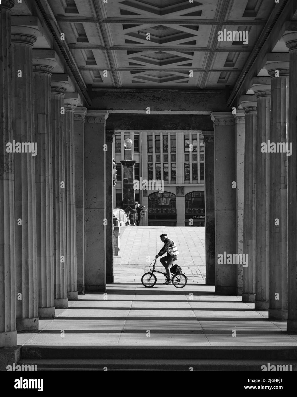 A grayscale shot of a cyclist between columns of Altes Museum in Berlin, Germany Stock Photo