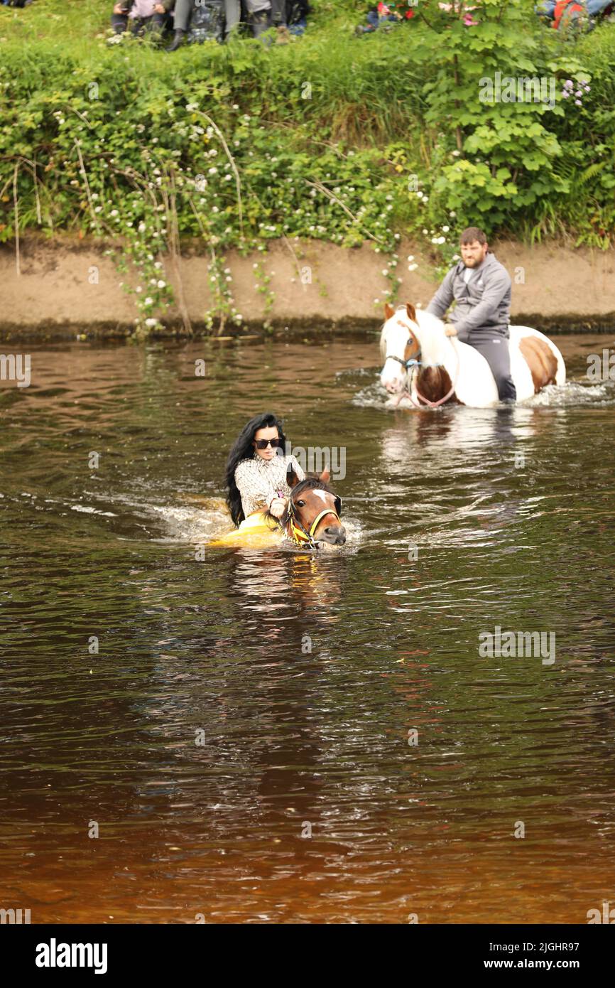 A young man and woman riding their horses through the River Eden, Appleby Horse Fair, Appleby in Westmorland, Cumbria Stock Photo