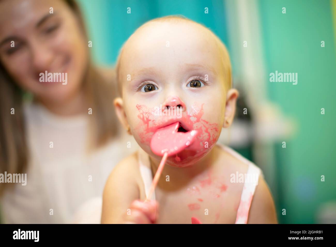 A little girl with a dirty face eats a candy and looks at the camera. Stock Photo