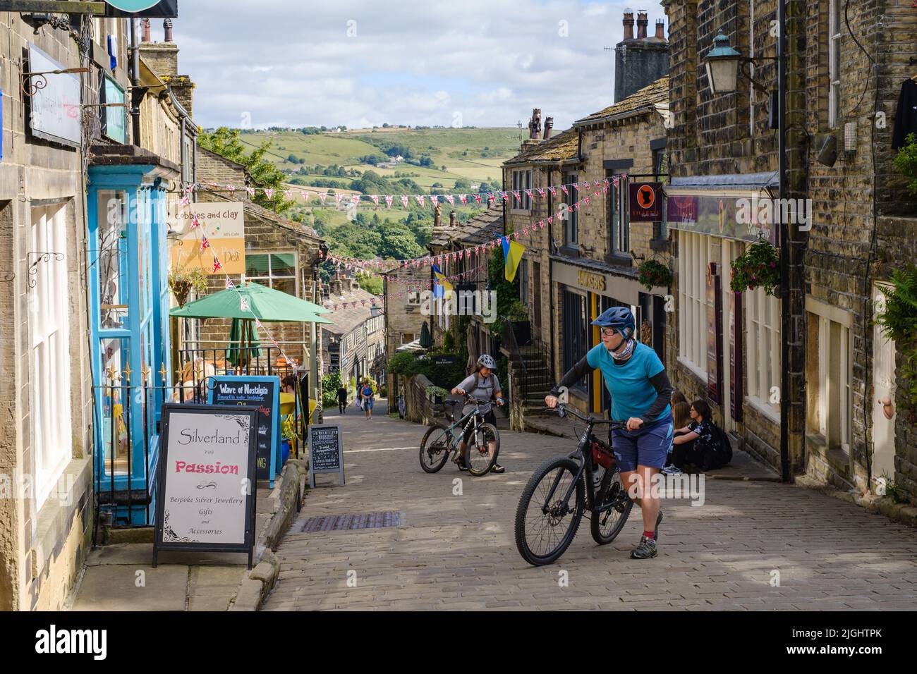Haworth, West Yorkshire, UK. Two cyclists pushing their bikes up the steep, Main Street hill in Haworth. Stock Photo