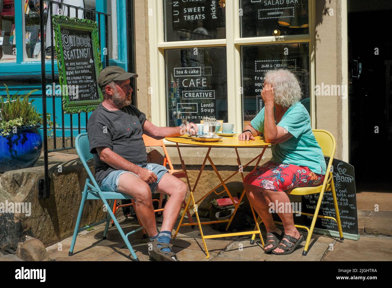 Haworth, West Yorkshire, UK. An elderly couple relaxing outside in the sunshine at a cafe on Main Street Haworth. Stock Photo