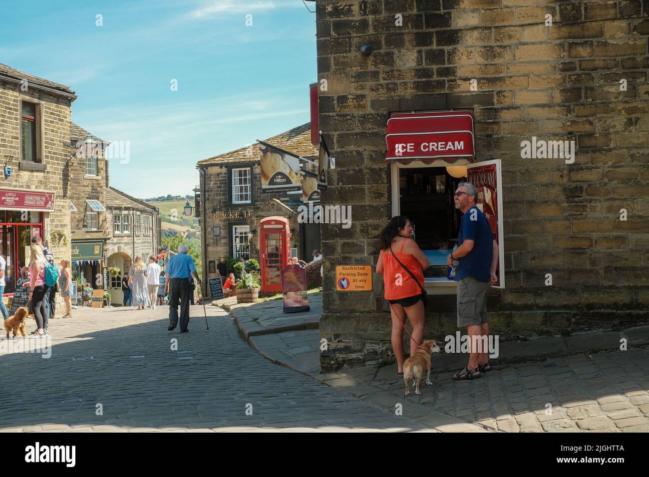 Haworth, West Yorkshire, UK. A couple buying an ice cream from a serving hatch at a cafe on Main Street Haworth on a warm Summer's day. Stock Photo