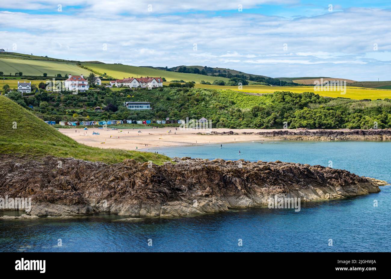View of Coldingham Bay with beach huts and people at seaside in Summer, Berwickshire, Scotland, UK Stock Photo